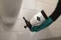 Preview: Anwendung des MESTO Cleaner 360° beim Sprühen unter einem Urinal – ideal für schwer zugängliche Stellen